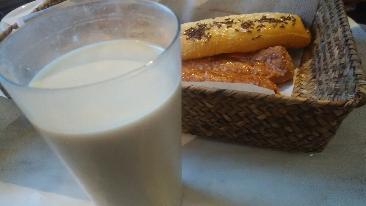 A tall glass of horchata de chufa next to a basket of fartons in Alboraya, near Valencia