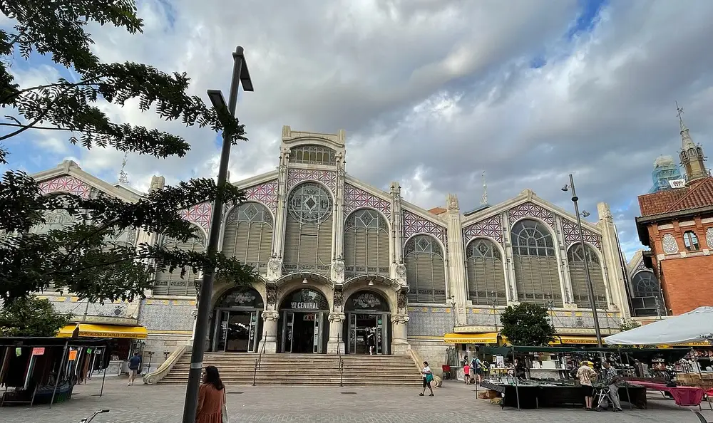 The main Modernista facade of Mercado Central in Valencia, MERCAT CENTRAL lettering above the entrance arches, market stalls set up on the square outside