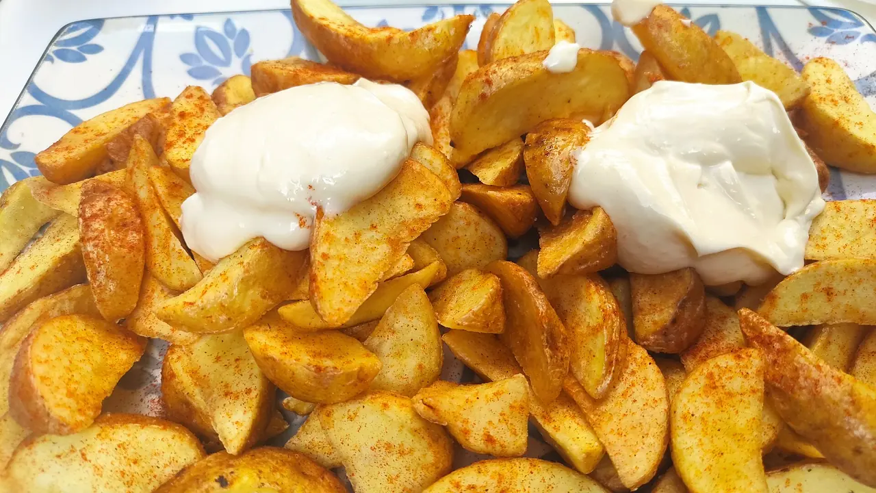 A plate of patatas bravas dusted with paprika and topped with two spoonfuls of alioli