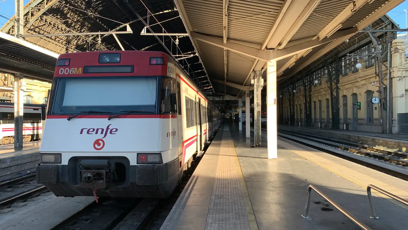 Un train de banlieue Renfe Cercanías rouge et blanc à quai sous la verrière métallique de l'Estació del Nord