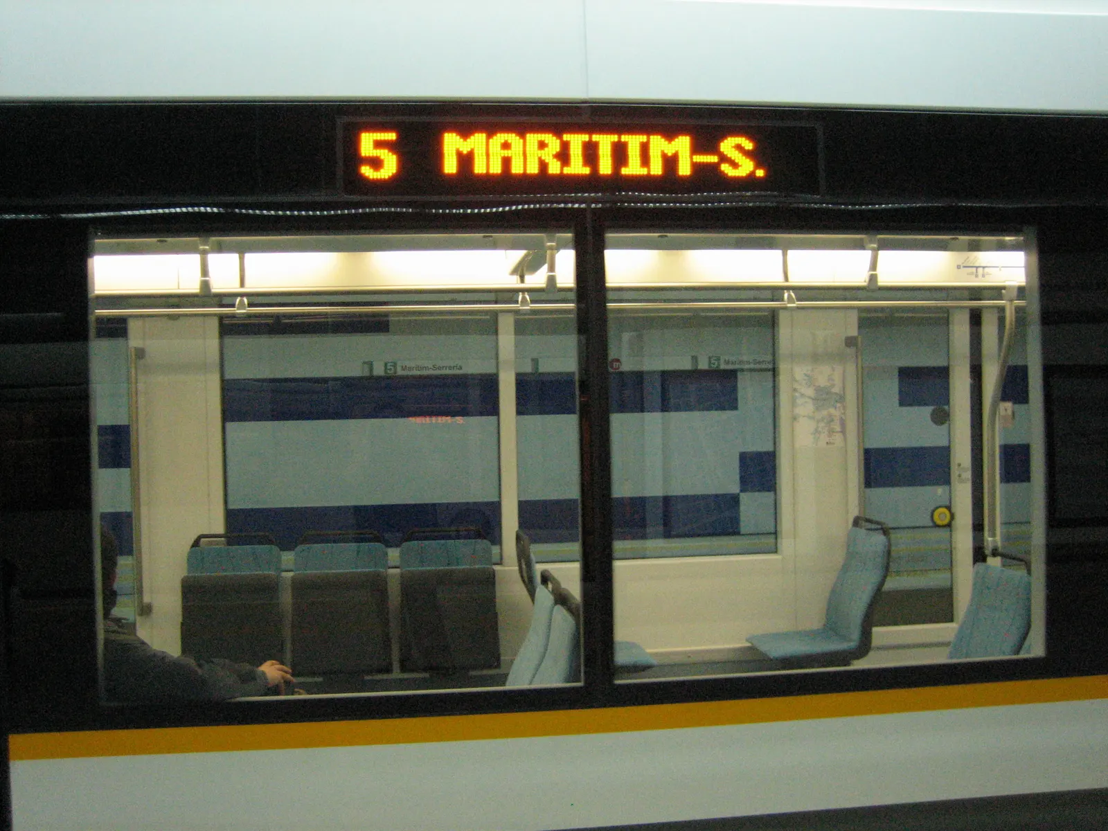 Un tren de la línea 5 de Metrovalencia en un andén subterráneo, con Marítim-Serrería en el indicador de destino