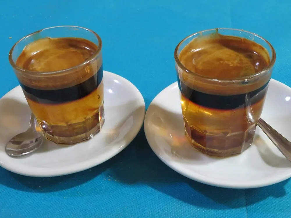 Dos vasos de carajillo cremat con capas de café y licor, con una cucharilla en el plato