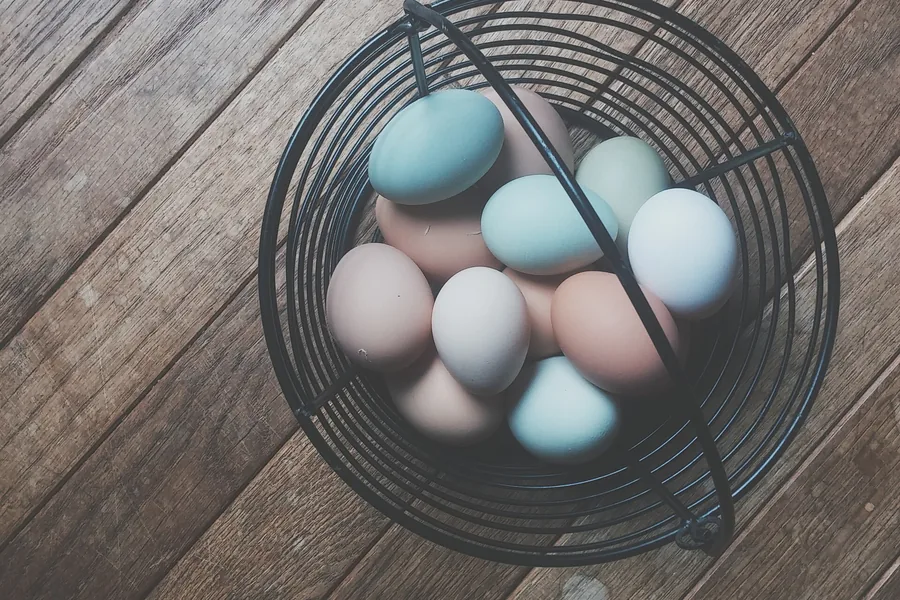 Pastel-coloured eggs of different shades in a black wire basket on a wooden floor
