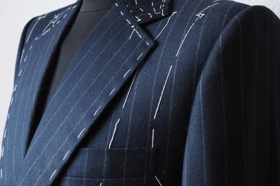 Close-up of a basted, unfinished pinstripe suit jacket on a tailor's mannequin, hand-stitched tacking visible