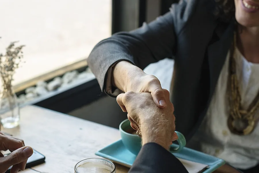 Close-up of two people shaking hands across a cafe table, coffee cups nearby