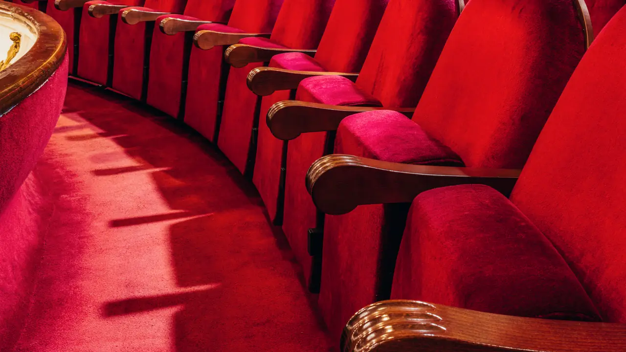 Una fila curva de butacas de teatro de terciopelo rojo bajo una luz cálida