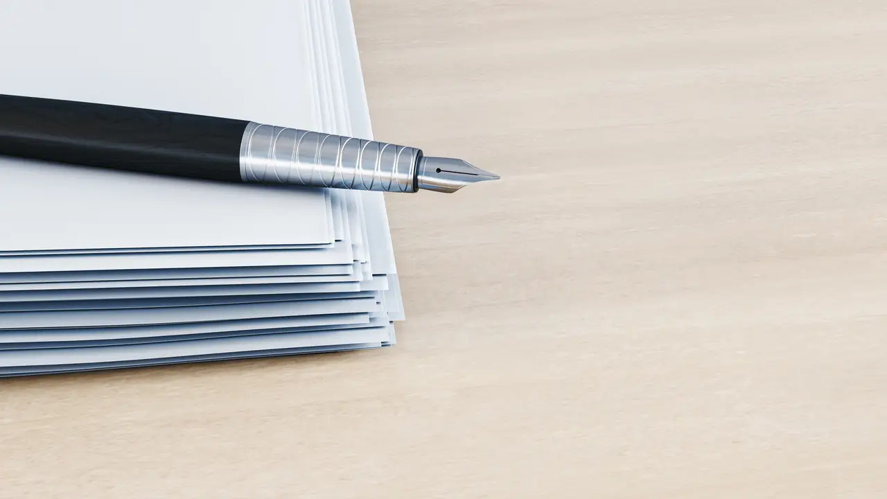 A fountain pen resting on a neat stack of blank paperwork on a sunlit wooden desk