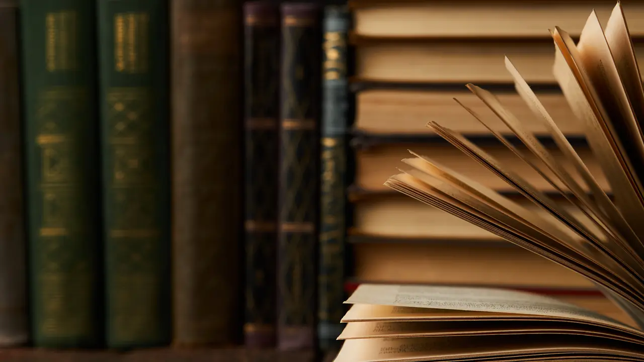 Une rangée de vieux livres reliés en cuir à côté d'un livre ouvert aux pages en éventail dans une lumière chaude